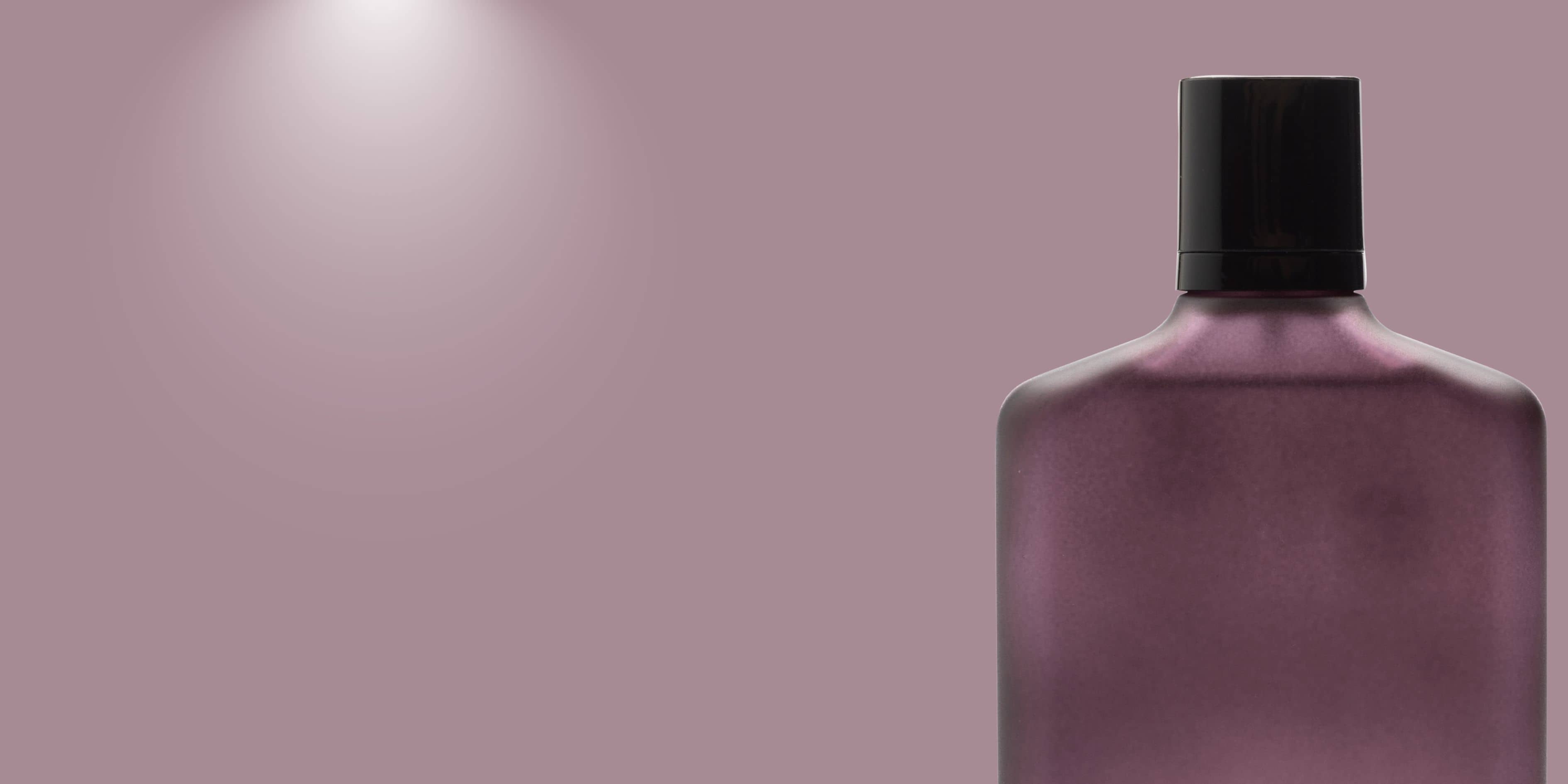 Matte mauve-purple perfume bottle with black cap, shown on a plain mauve background under a soft spotlight.